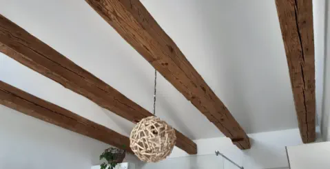 Altholzbalken aus Fichte mit original handgehackter Oberfläche an der Schlafzimmerdecke unter der Dachschräge
