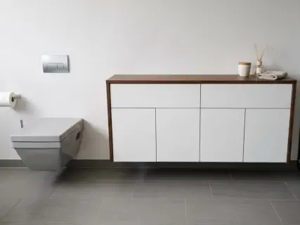 Weißer Badschrank mit Holzrahmen als Sideboard neben dem Wand-WC