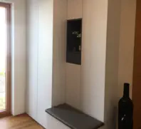 Grifflose Einbauschrankwand in hellem Farbton mit dunkler offener Nische und grauer Sitzbank