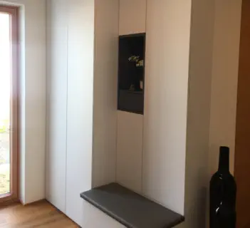 Grifflose Einbauschrankwand in hellem Farbton mit dunkler offener Nische und grauer Sitzbank