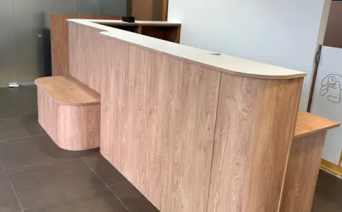 Geschwungene Empfangstheke nach Maß in Holz mit indirekter LED-Beleuchtung