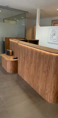Geschwungene Empfangstheke in Holz mit indirekter LED-Beleuchtung und niedriger Ablage für Besucher