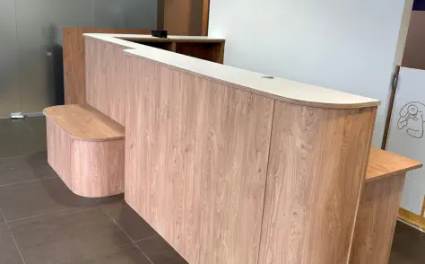 Geschwungene Empfangstheke nach Maß in Holz mit indirekter LED-Beleuchtung