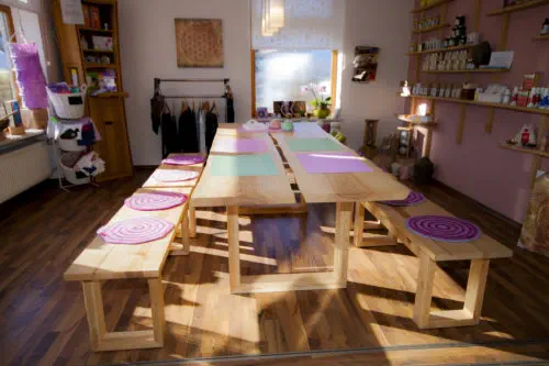 Lange Tafel aus massiven Baumkantenplatten mit passenden Sitzbänken in einem Laden- und Kursraum