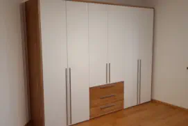 Weißer Kleiderschrank mit langen Edelstahlgriffen, Holzschubladen in der Mitte und seitlicher Holzwange