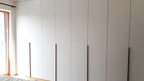 Weißer Kleiderschrank über die ganze Wandbreite, grifflos mit schwarzen senkrechten Griffleisten