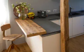 Kleine Frühstückstheke aus Altholz an grauer Arbeitsplatte, daneben ein alter Holzbalken als Stütze