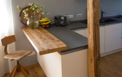 Kleine Frühstückstheke aus Altholz an grauer Arbeitsplatte, daneben ein alter Holzbalken als Stütze