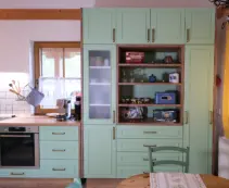 Weiße grifflose Küche in L-Form mit beleuchtetem Wandbord, eingebautem Backofen und heller Arbeitsplatte