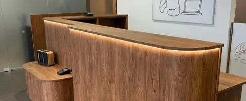 Geschwungene Empfangstheke nach Maß in Holz mit indirekter LED-Beleuchtung
