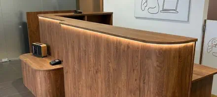 Geschwungene Empfangstheke nach Maß in Holz mit indirekter LED-Beleuchtung