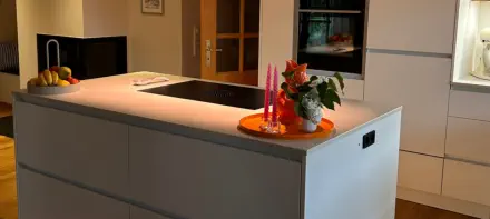 Küche nach Maß mit grauer Kochinsel, warm leuchtender LED-Sockelbeleuchtung und hellen Hochschränken