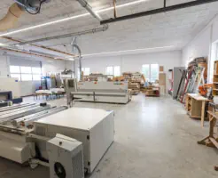 Blick in die erweiterte Werkstatt mit Maschinen zur Plattenbearbeitung und Holzlager